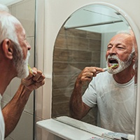Older man with dental implants in Lewisville brushing his teeth