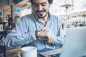 Smiling man at laptop checking watch