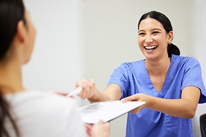 A dental assistant handing a patient a dental insurance form