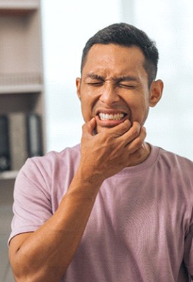 Man in pink shirt squinting eyes and touching corners of mouth in pain