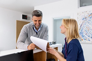 a dental patients speaking with a front desk staff member and looking at papers