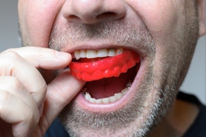 close up of man with facial hair putting in red mouthguard