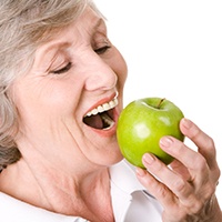 Senior woman enjoying an apple with the help of dental implants