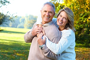 Older couple with dental implants in Lewisville smiling and hugging