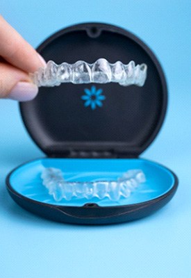 Fingers lifting Invisalign tray out of carrying case with light blue background