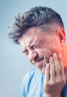 Man with gray hair squinting and touching jaw in pain