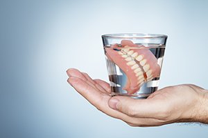 Hand holding glass of water with dentures inside