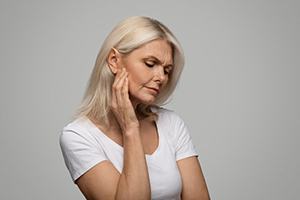 a woman touching her cheek due to failed dental implant