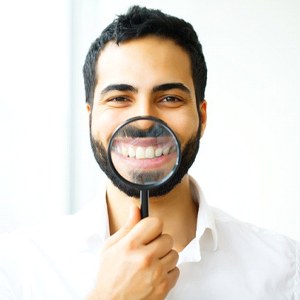 man holding magnifying glass to his smile with veneers in Lewisville