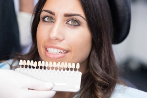 woman smiling while dentist holds veneers in front of her face