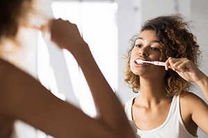 person brushing their teeth while looking in the bathroom mirror