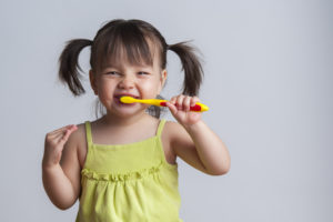 Smiling little girl in pigtails brushing her teeth