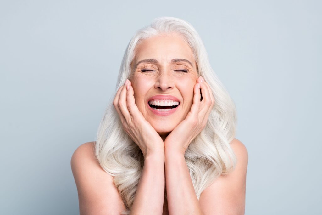 Woman with white hair smiling with eyes closed touching her cheeks