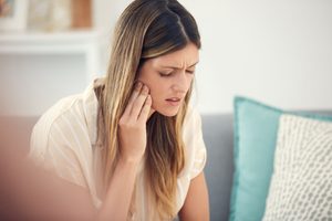 Woman on couch pressing hand to jaw in pain