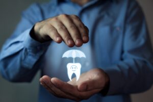 Man holding digitally illuminated tooth covered by insurance umbrella.